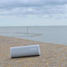 SONOS Roam in white on a sea wall with the sea in the background.