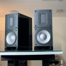 A pair of Raidho Acoustics X1t Loudspeakers in black on a white circular table